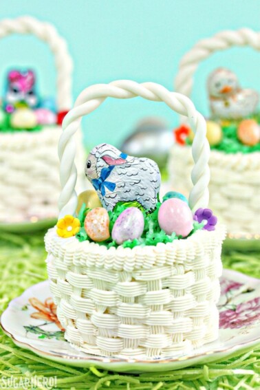 Close of up an Easter Basket Cupcake on a small round plate with floral design and two other Easter basket cupcakes in the background.
