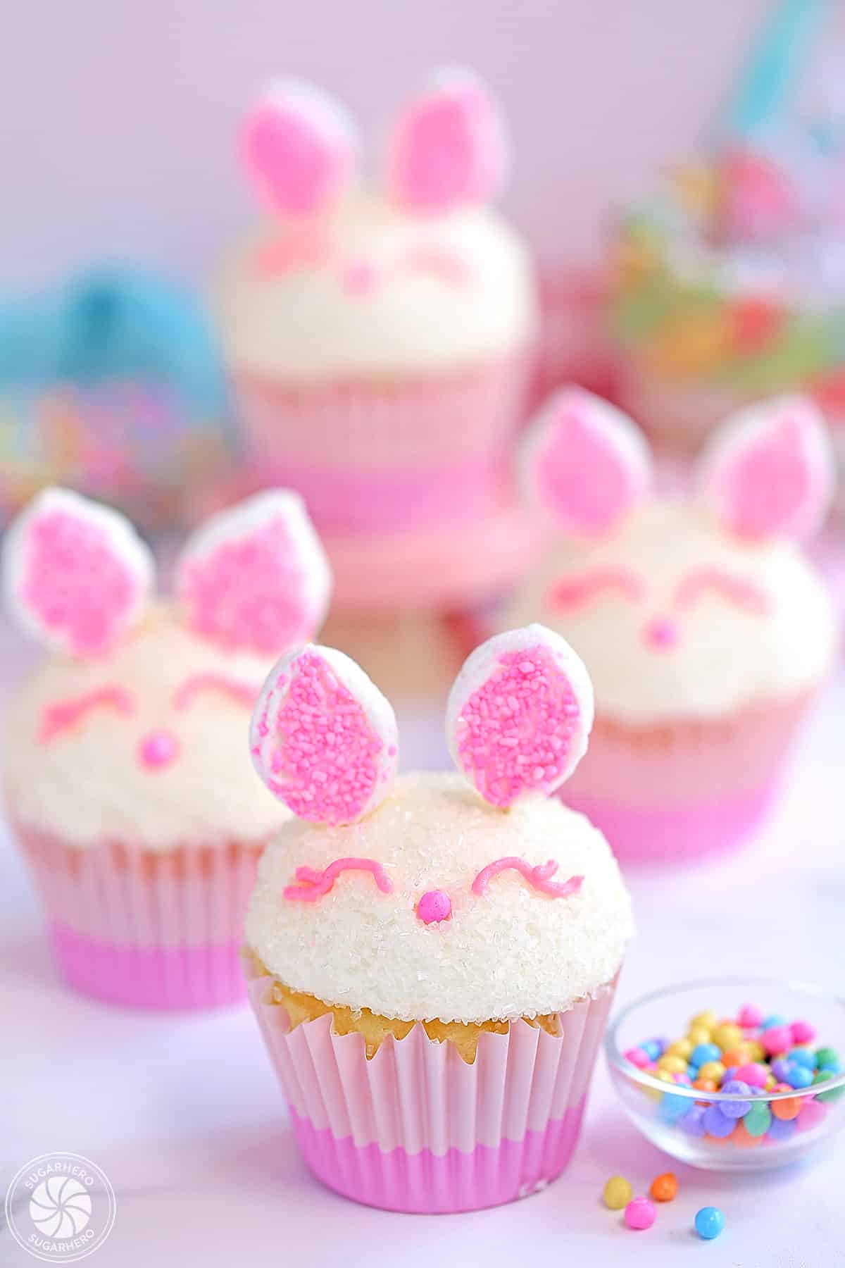 4 Easter Bunny Cupcakes next to a small bowl of sprinkles.