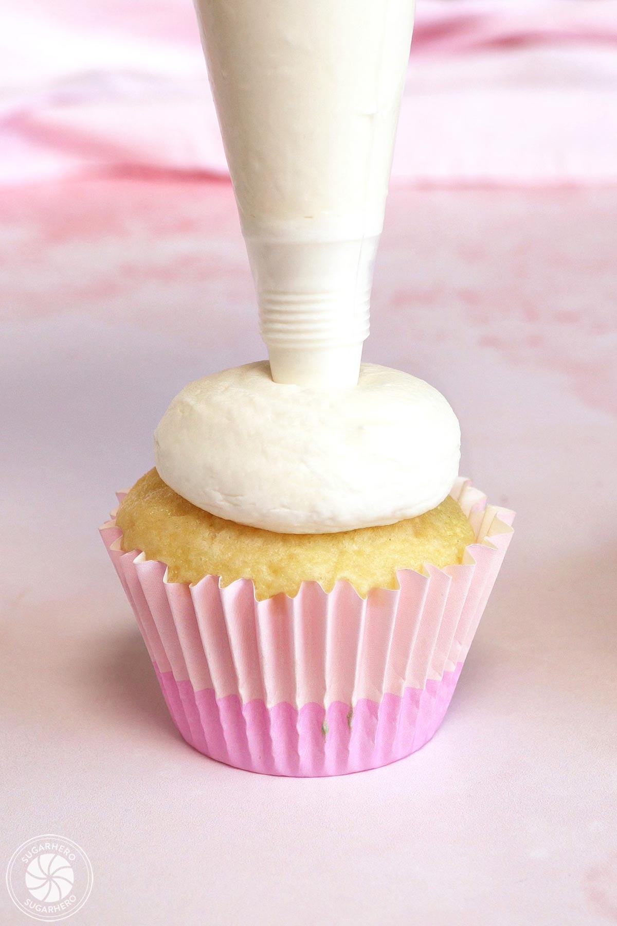 Piping a big mound of white buttercream on top of a cupcake.