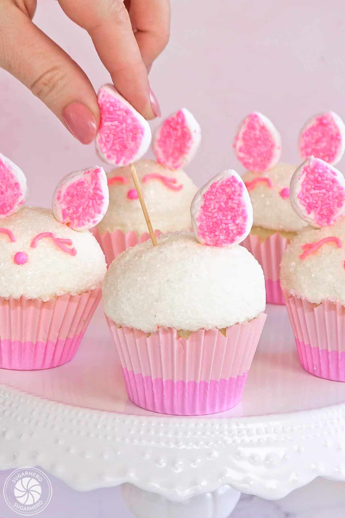 Adding a marshmallow ear on a skewer to bunny cupcakes.