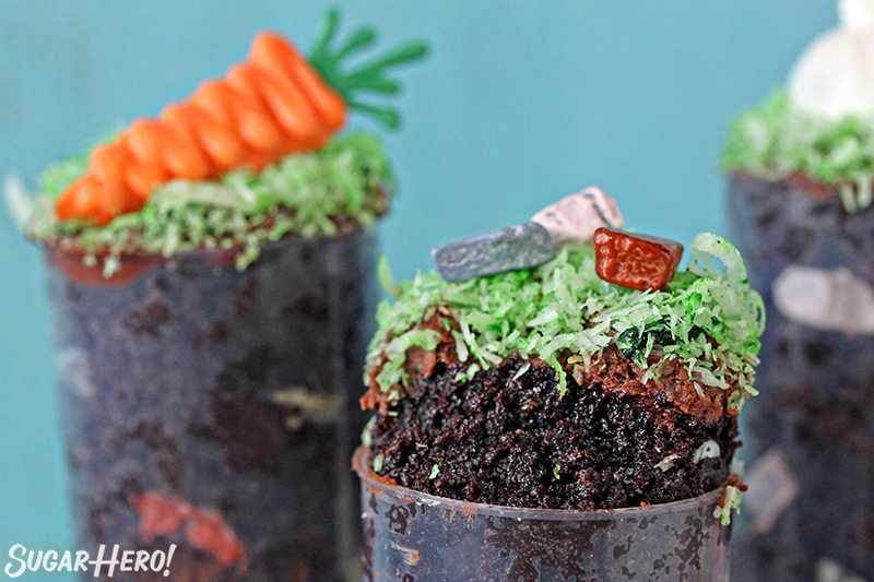 Two Easter push-up pops filled with chocolate cake, one is topped with bunny ears and one is topped with chocolate rocks.