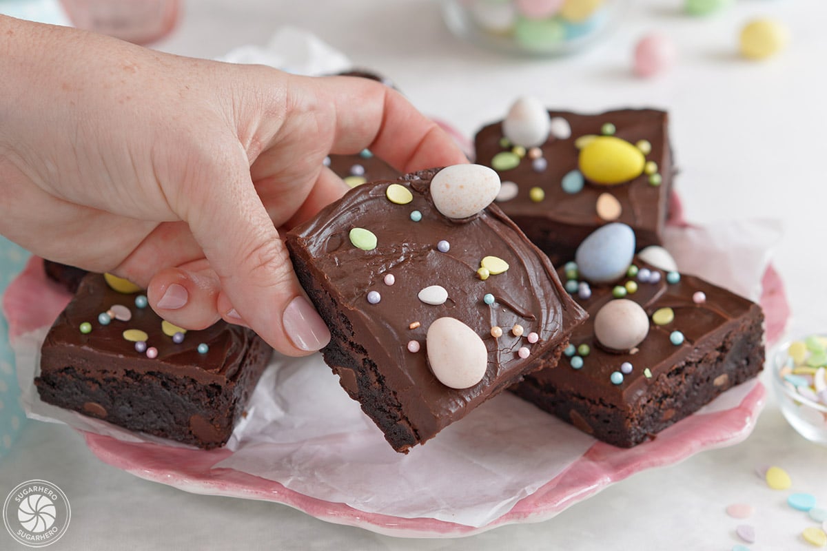 Hand holding up a brownie with chocolate frosting and chocolate eggs on top.