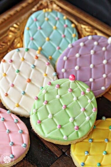 A pile of Fondant-Covered Easter Egg Cookies on a wooden surface.