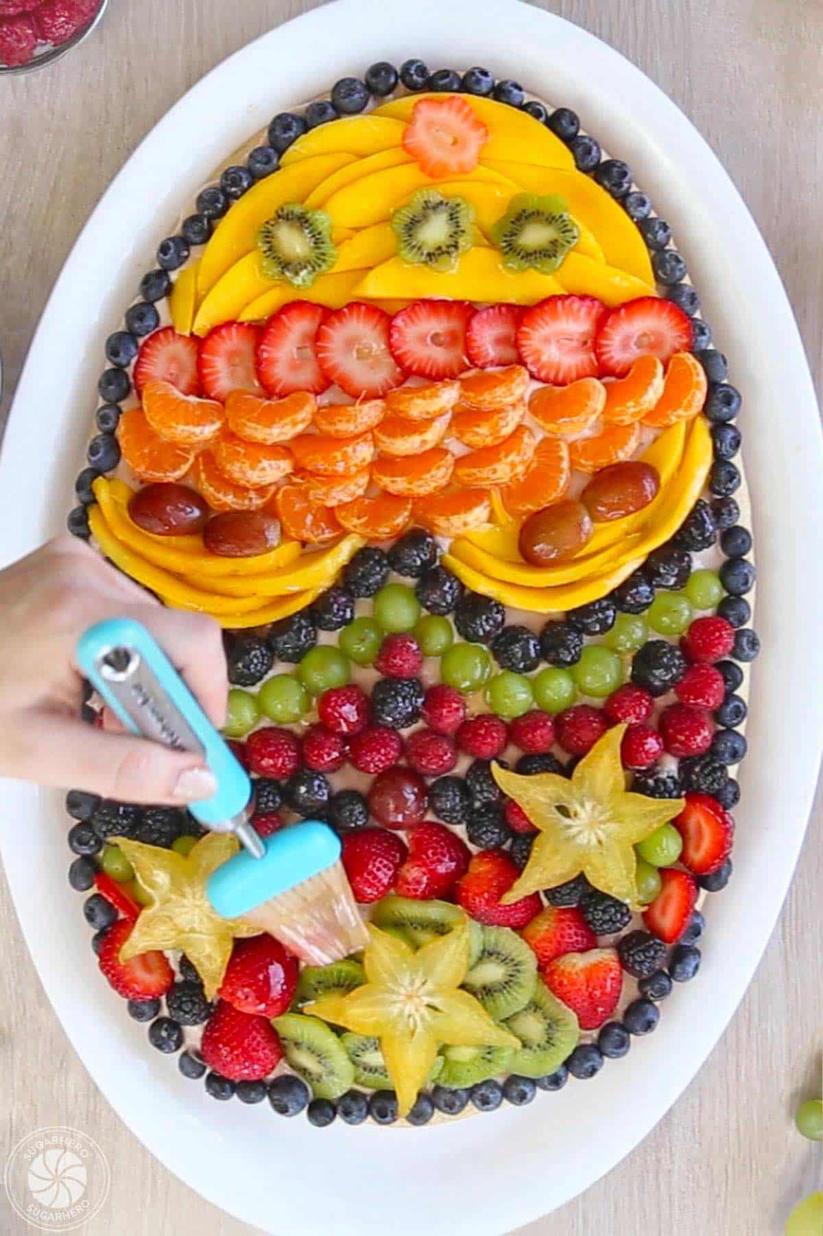 Hand brushing glaze to the top of an Easter egg fruit pizza.