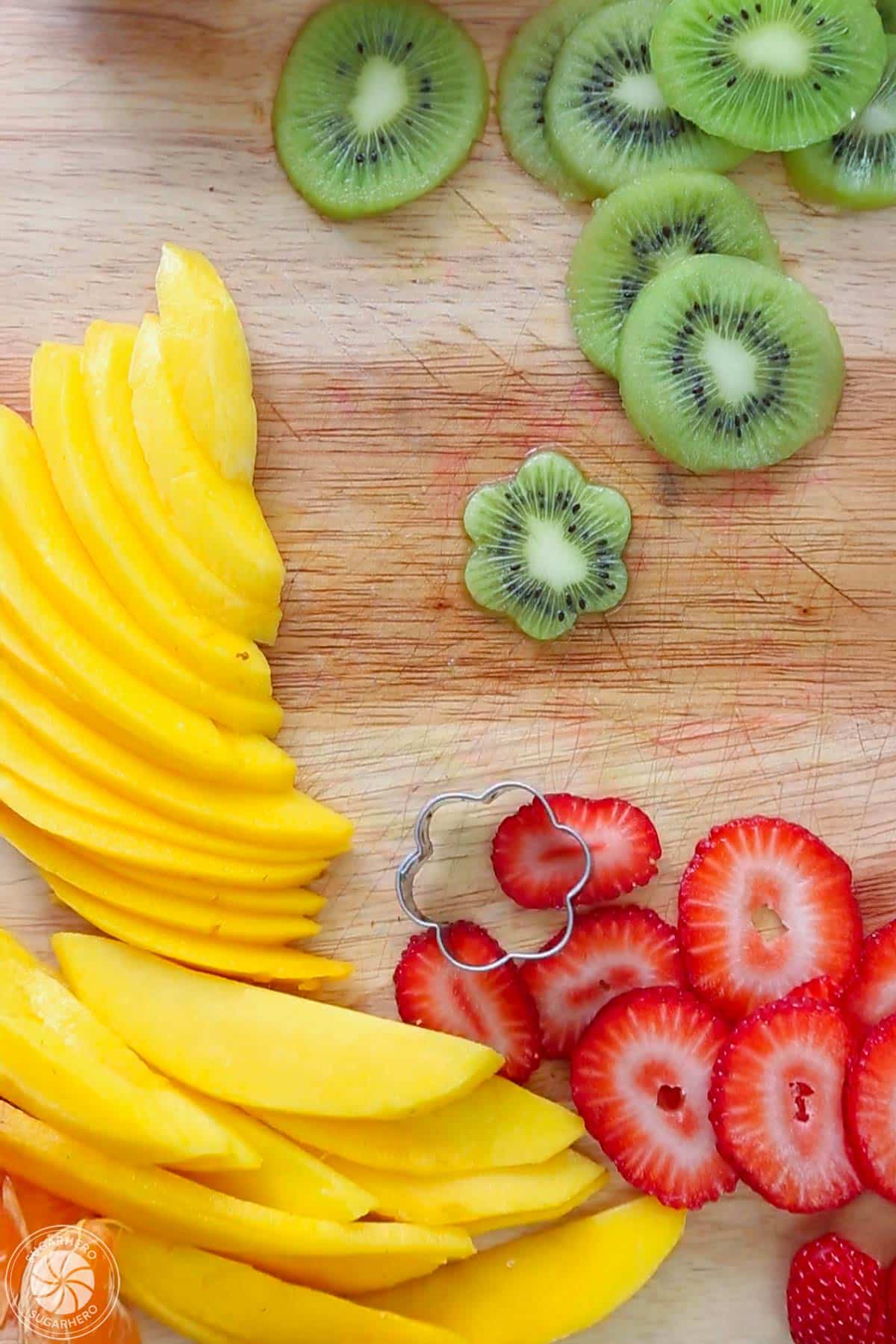Sliced mangoes, strawberries and kiwis on a cutting board.