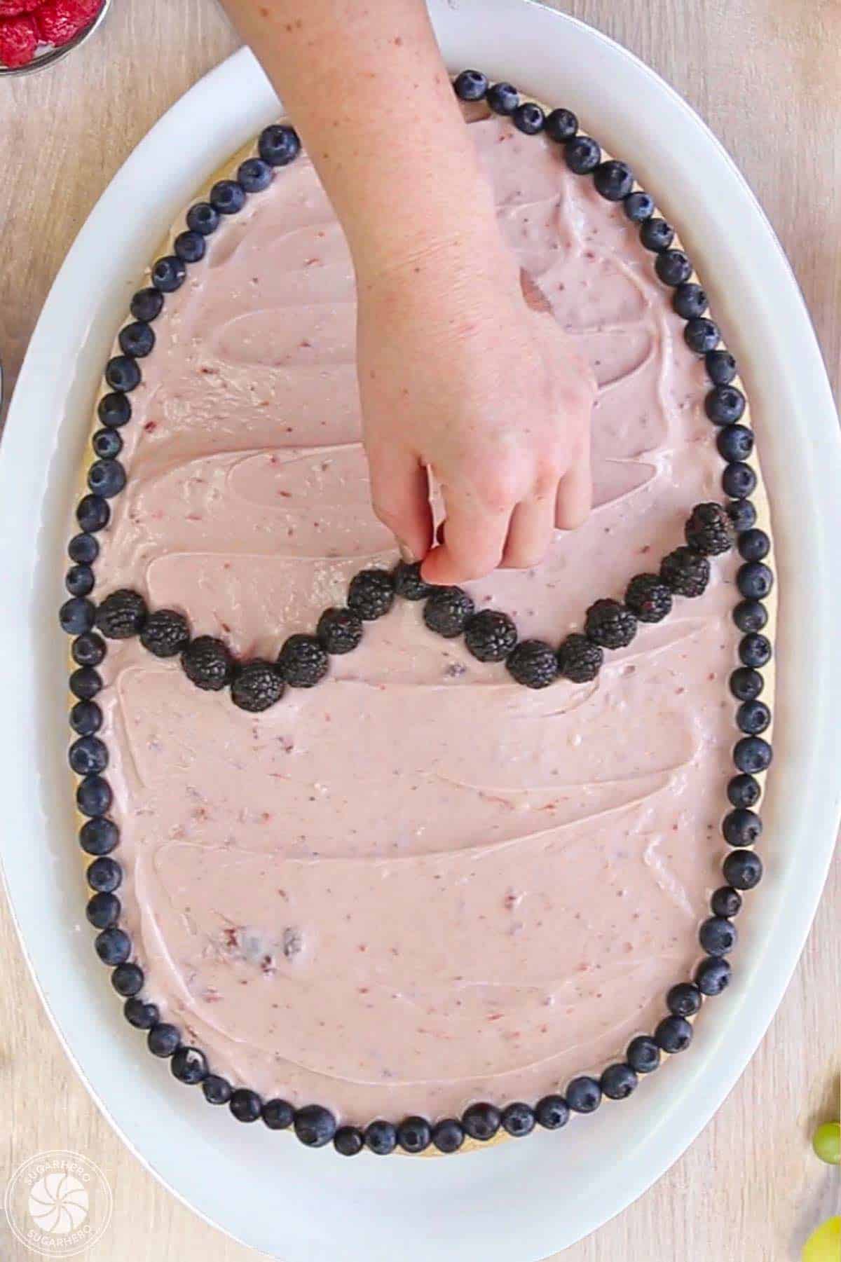 Hand placing berries on top of a frosted fruit pizza to make an egg design.