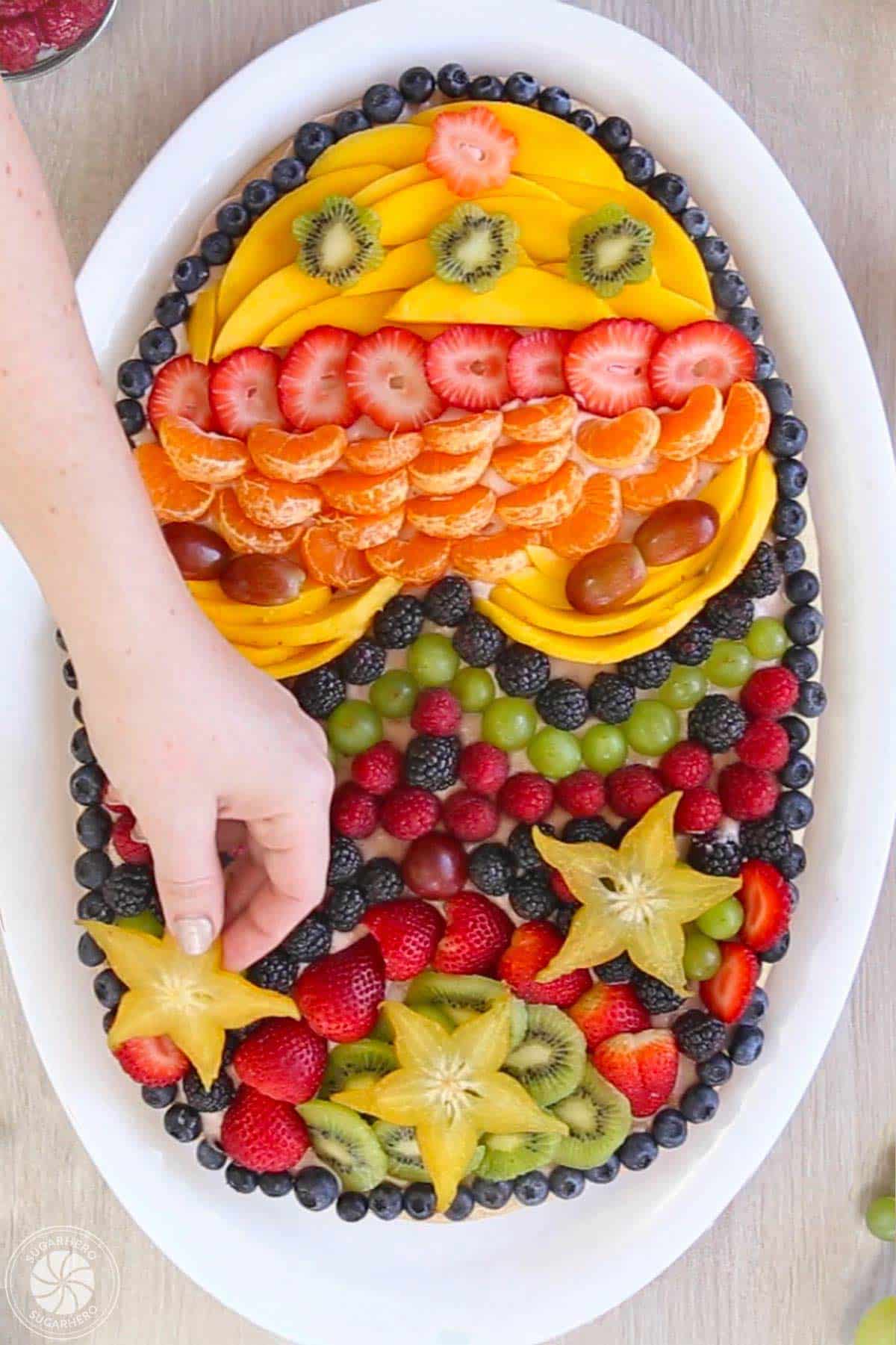 Hand placing a slice of star fruit to the top of a decorated Easter fruit pizza.
