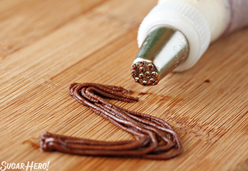 Grass piping tip piping chocolate buttercream on a wooden surface.