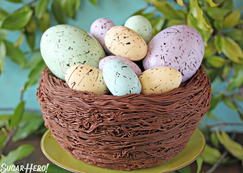 Close up of Easter Nest Cake on a green cake stand surrounded by greenery.