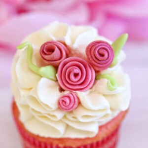 Close up of cupcake with white ruffled frosting and pink fondant flowers.