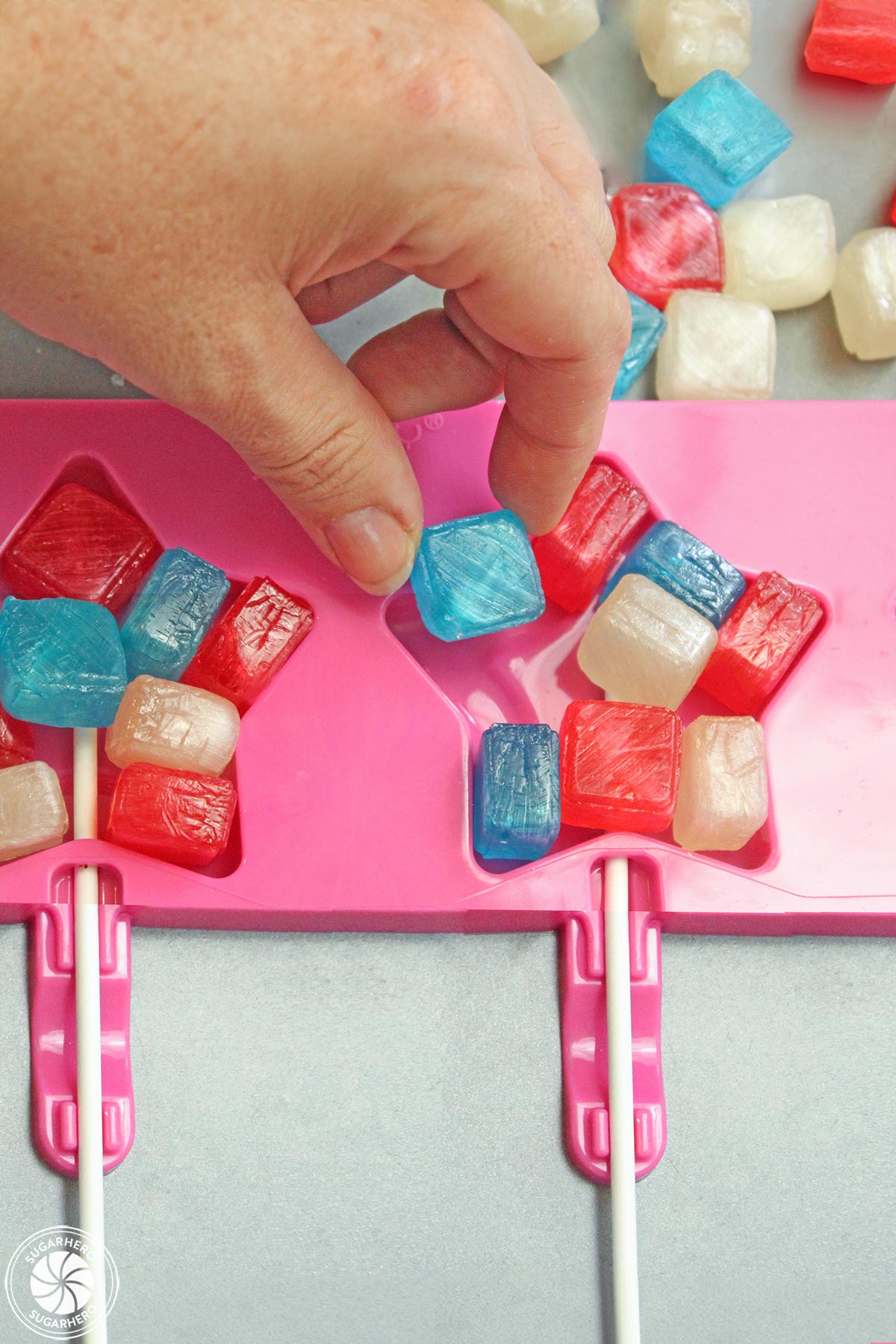Hand placing colorful hard candy in a star lollipop mold.