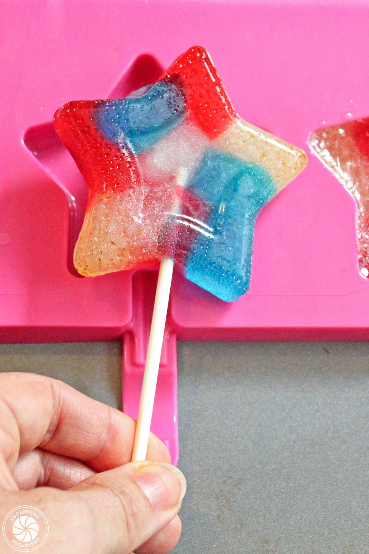 Hand holding up a multi-colored star lollipop.