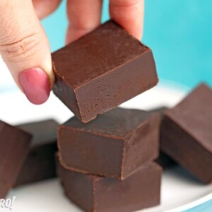 Hand picking up a piece of chocolate fudge from a white plate.