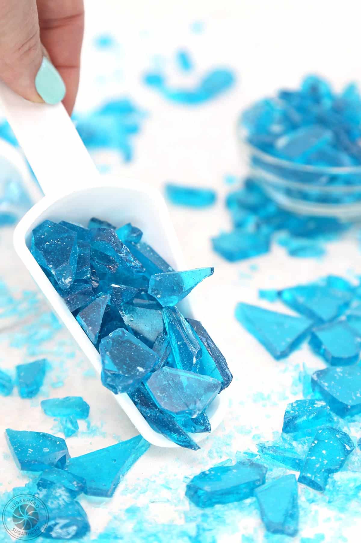 Hand holding a white scoop filled with blue candy glass.