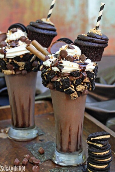 2 Epic Chocolate Peanut Butter Milkshakes on a counter next to a stack of cookies.