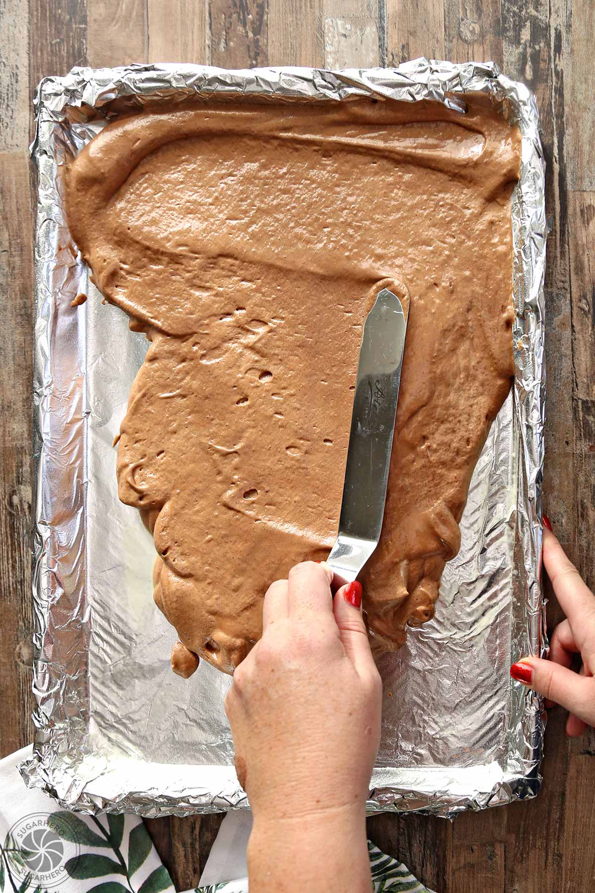 Using an offset spatula to spread the cake batter into a foil-lined, greased baking shett.