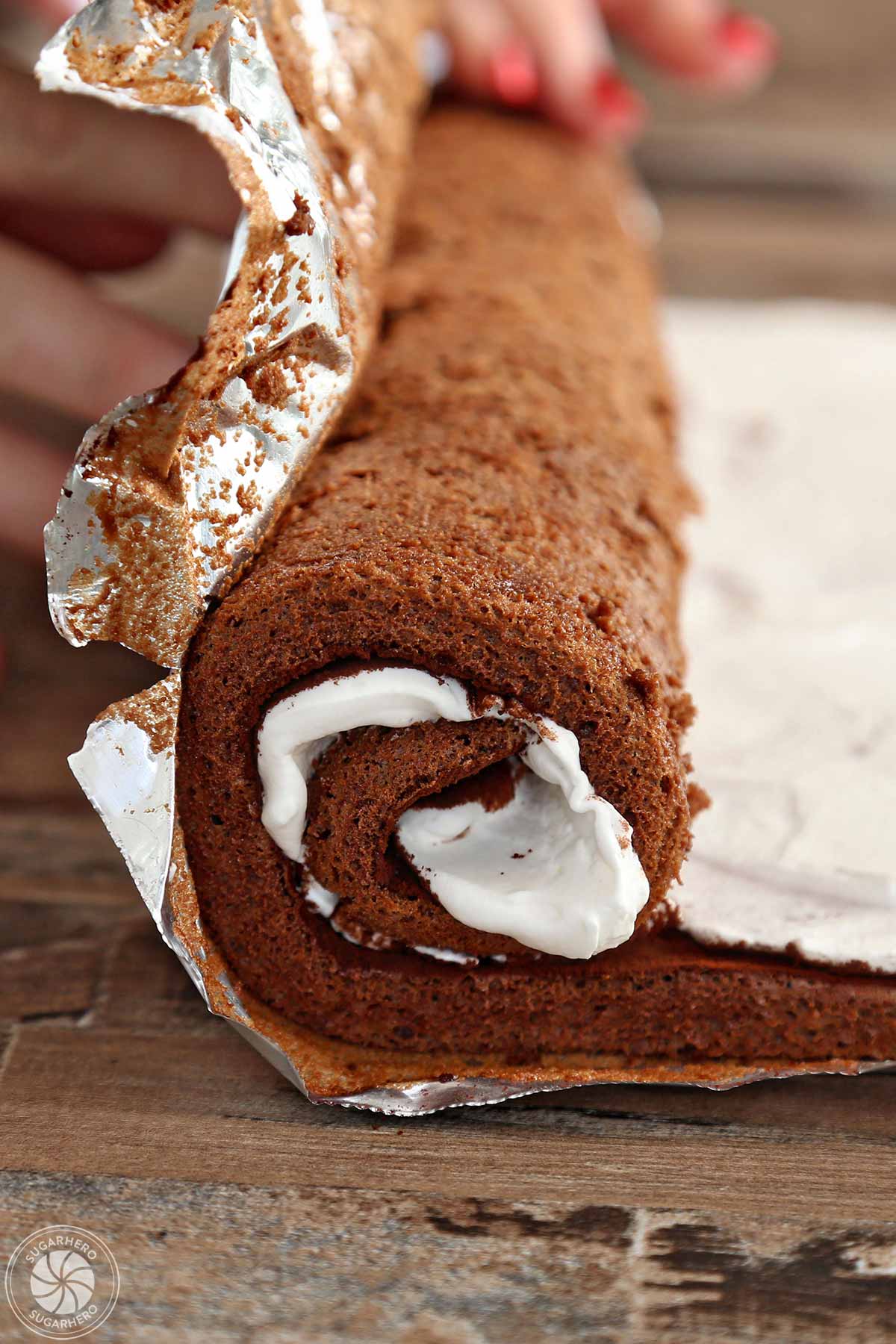 Rolling a flourless chocolate cake filled with whipped cream into a spiral shape.