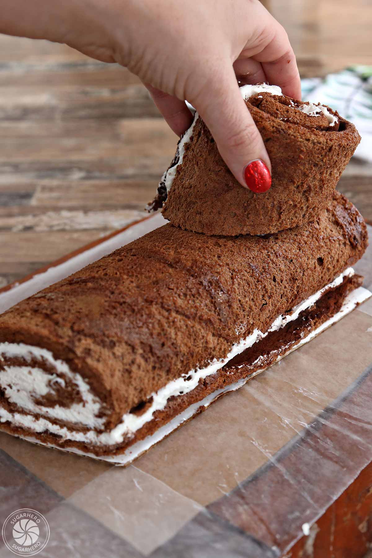 Placing a small piece of cake on top of the rest of the cake roll to make the shape of a log.