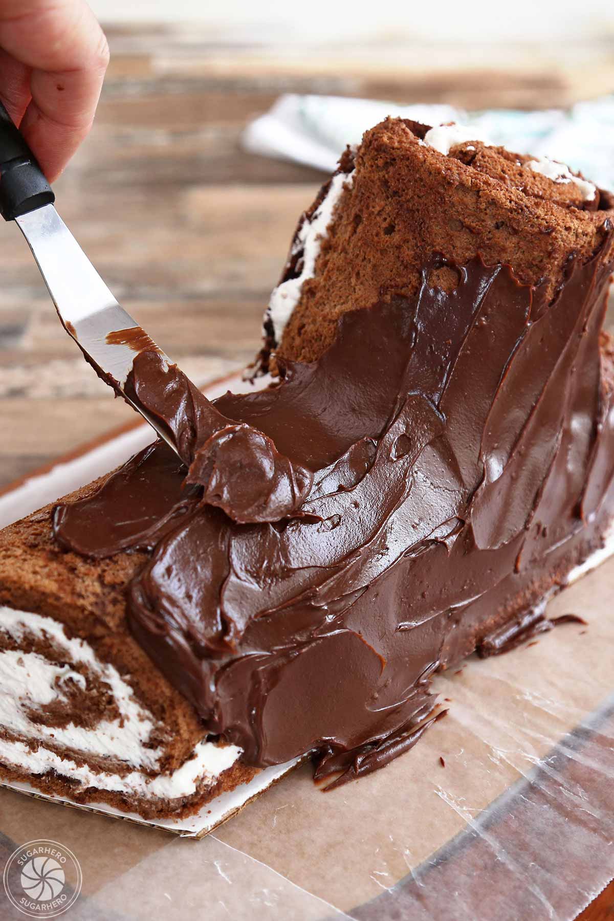 Using a spatula to spread cooled ganache on the outside of the Flourless Chocolate Buche de Noel.