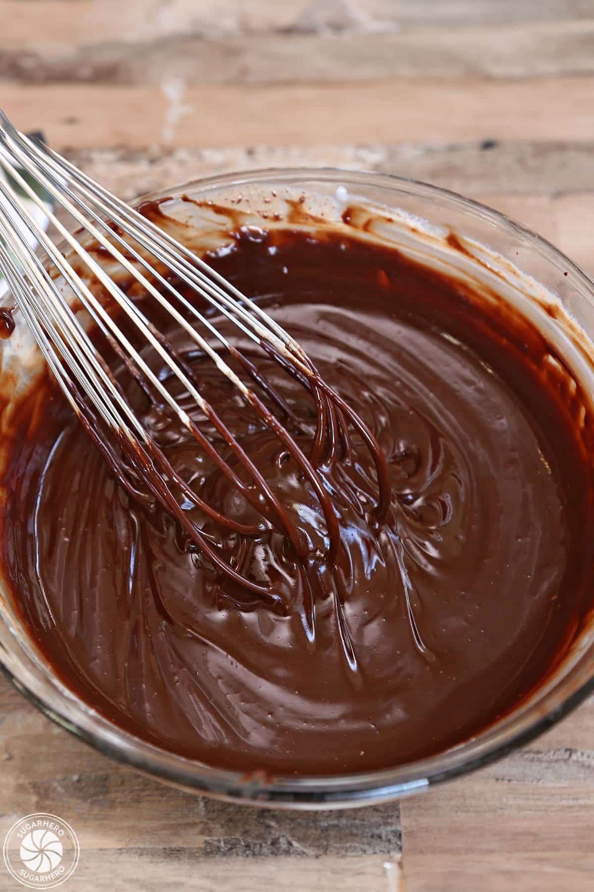 Glossy chocolate ganache in a mixing bowl with a wire whisk in it.