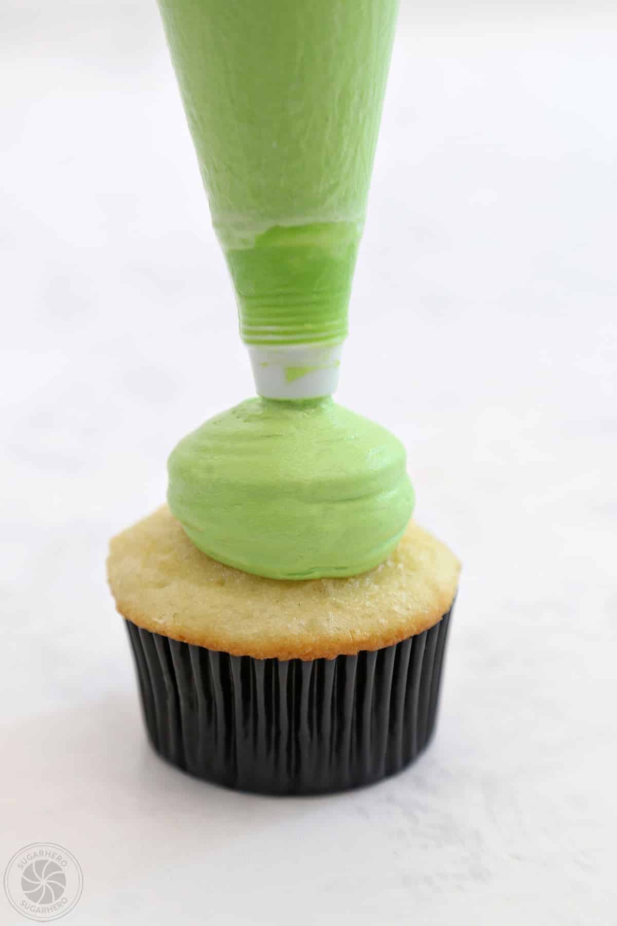 Green frosting being piped onto a cupcake.