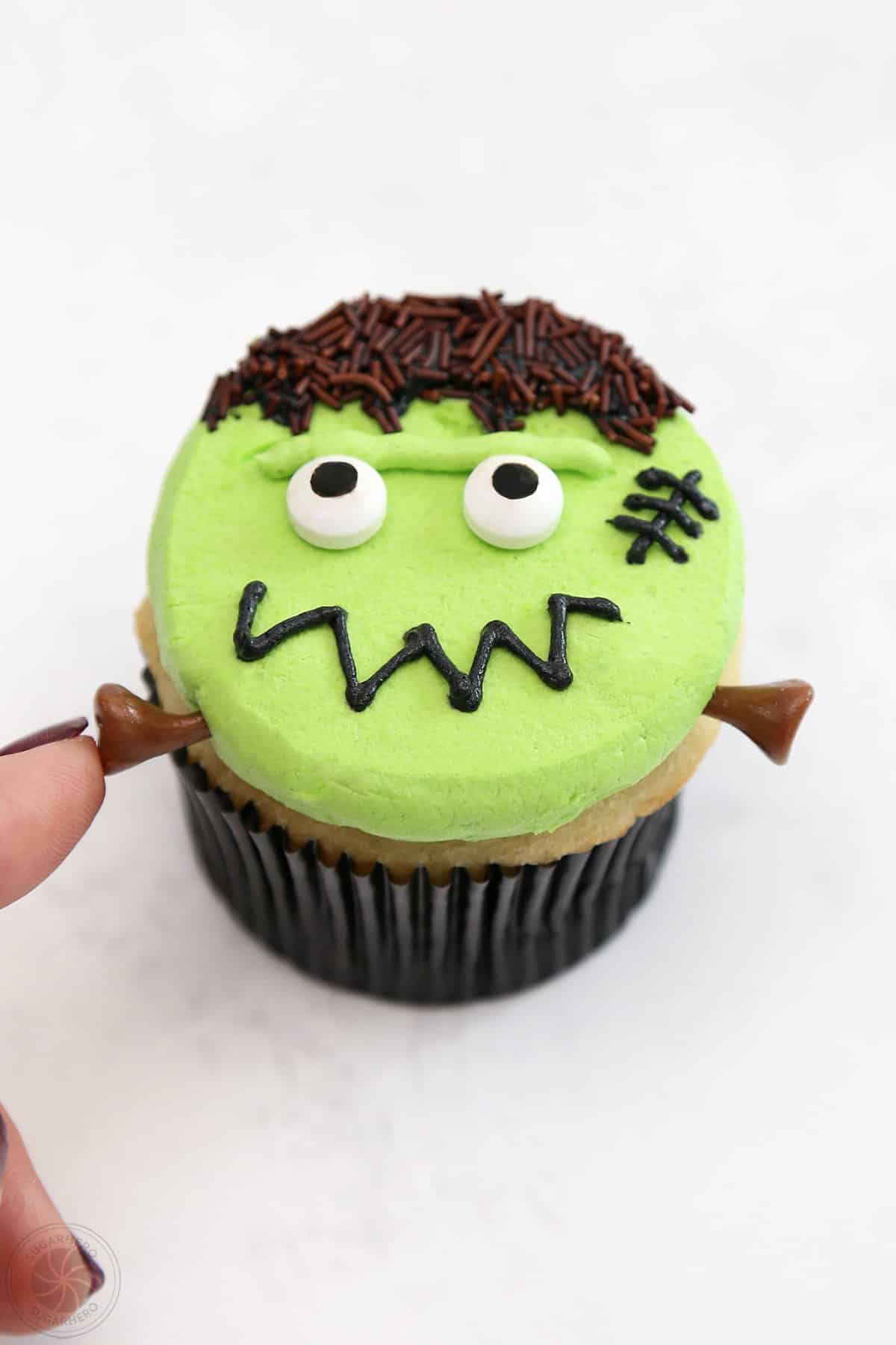 Finger pressing candy neck bolts on a Frankenstein Cupcake.