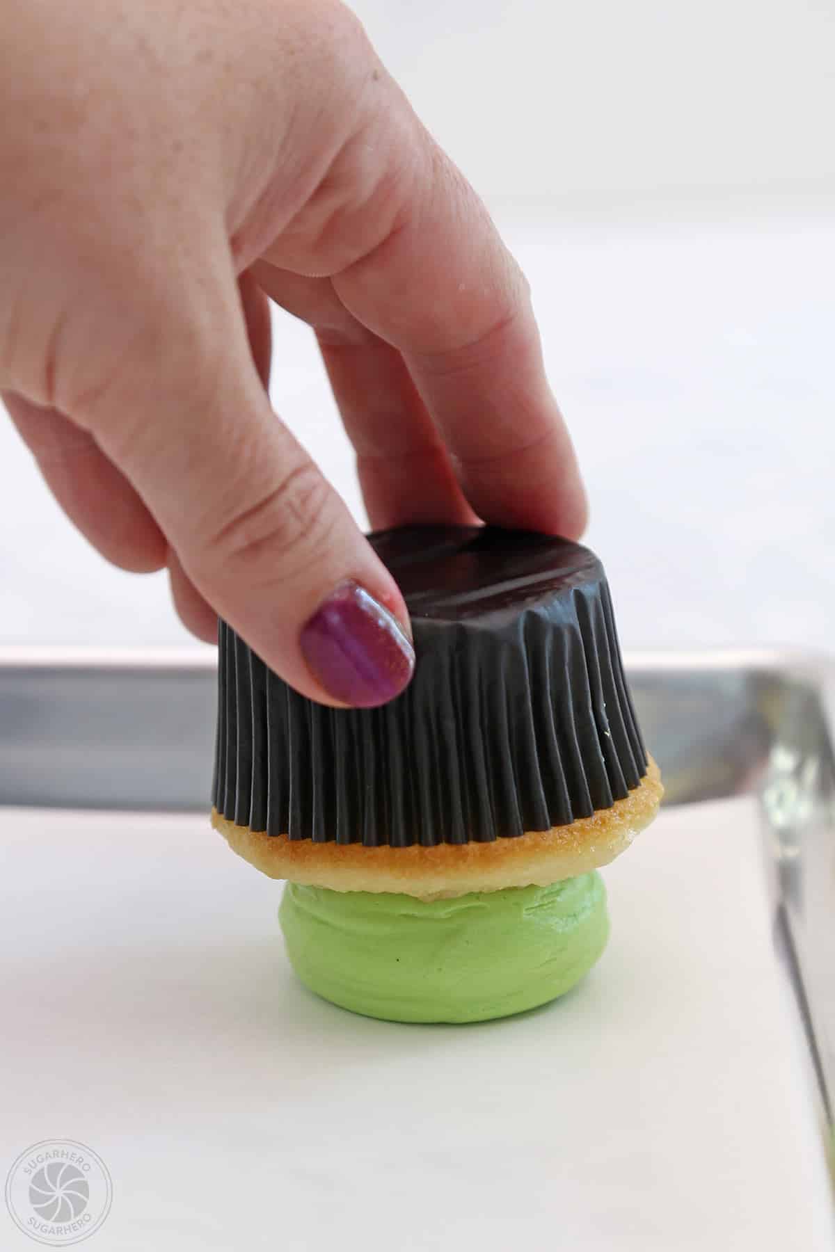 Hand pressing a cupcake upside down on parchment paper to flatten the buttercream.