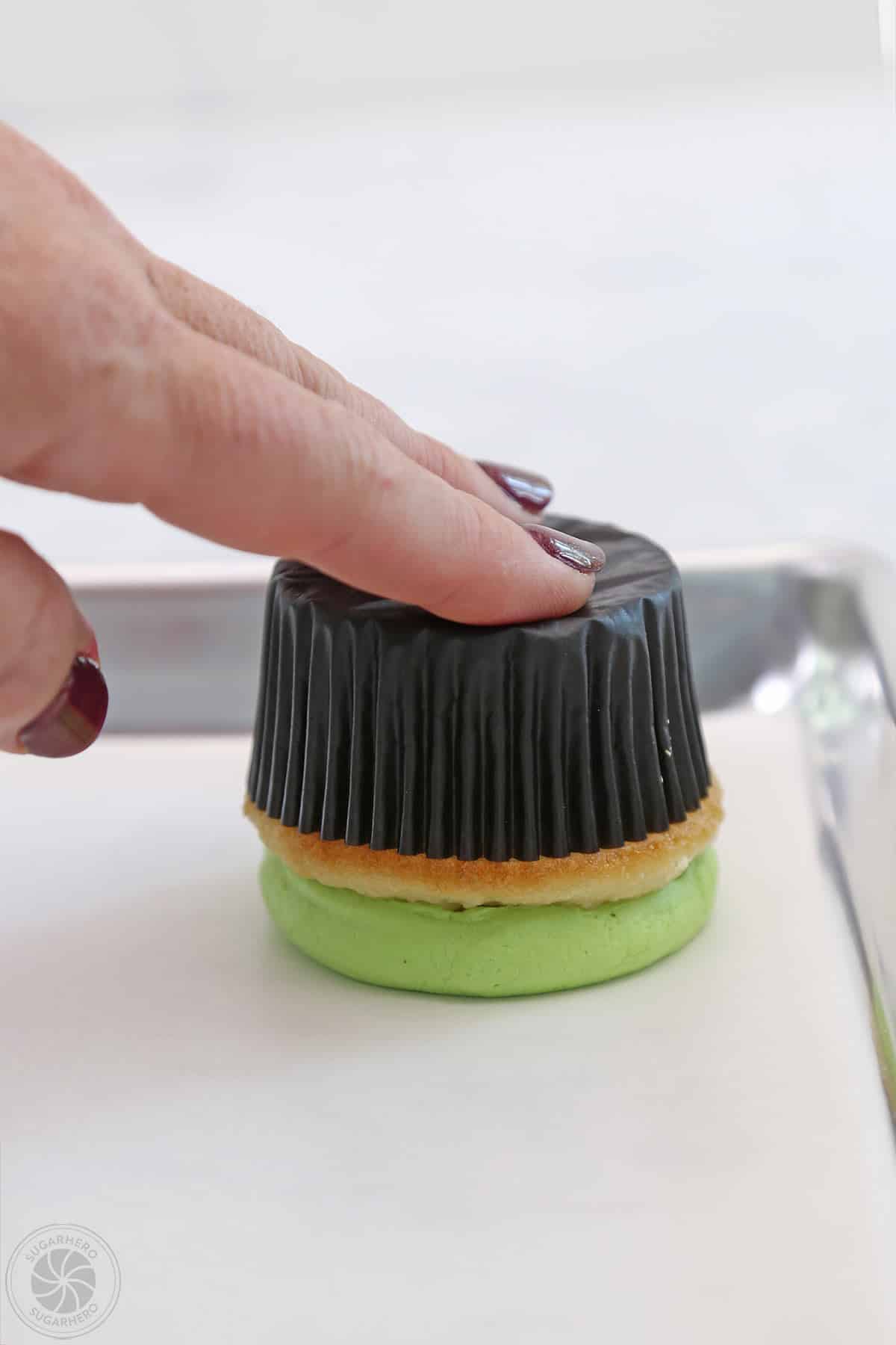 Hand pressing an upside down cupcake to flatten the buttercream.