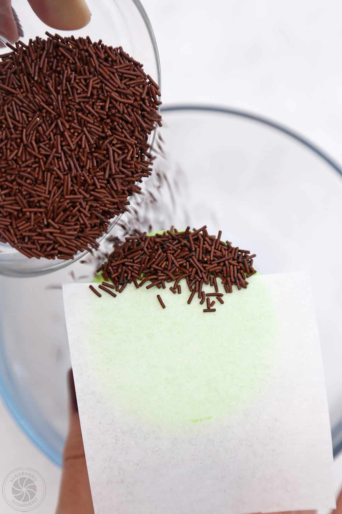 Bowl sprinkling brown sprinkles on top of a Frankestein Cupcake to look like hair.