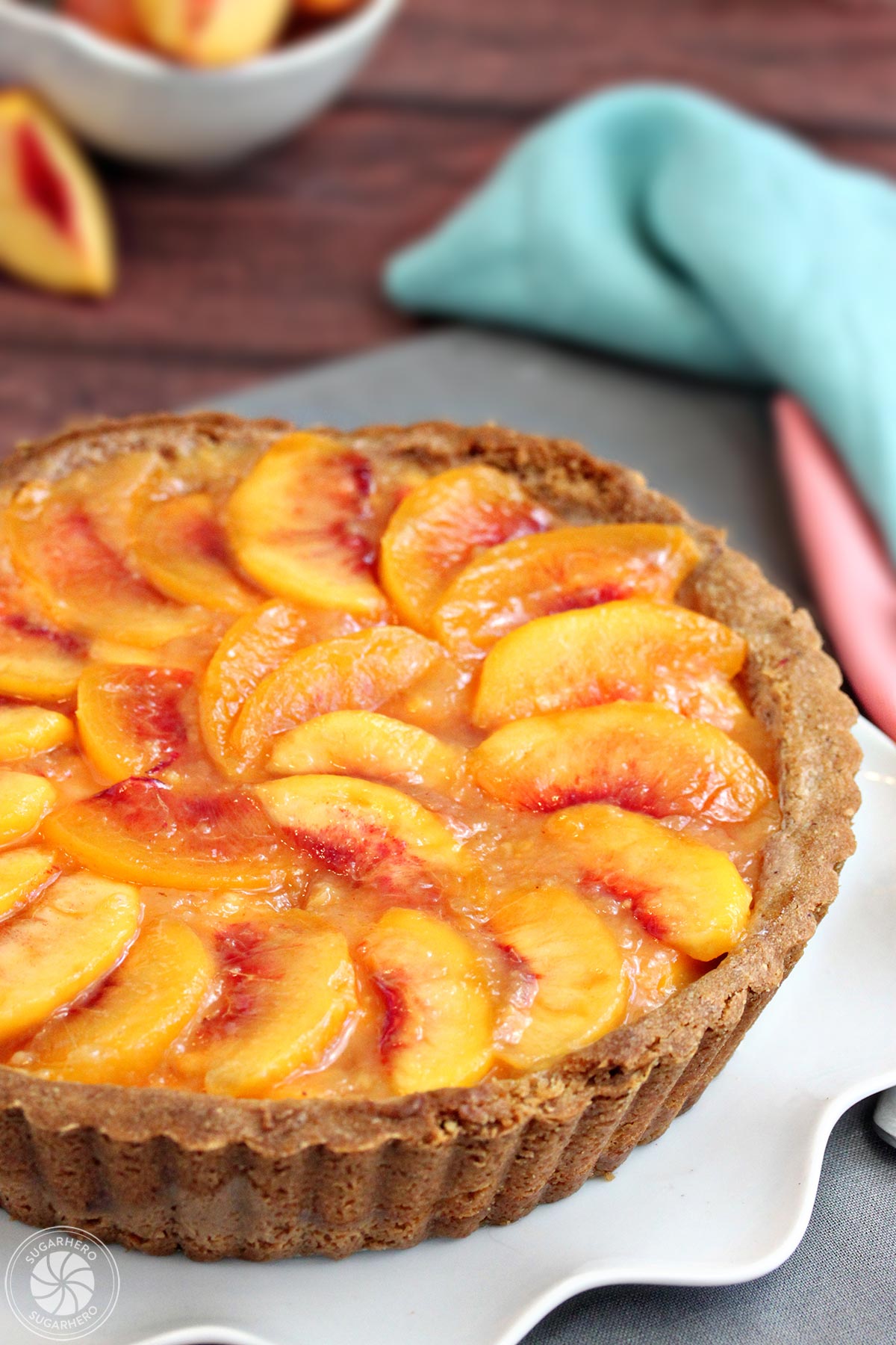 Vertical image of a no-bake Fresh Peach Tart with peaches in the background | From SugarHero.com