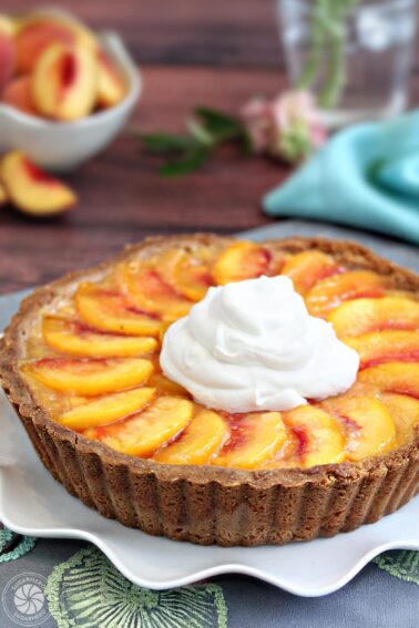 Close up of a Fresh Peach Tart with a large dollop of whipped cream on top.