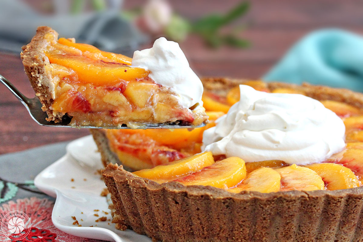 Lifting out a slice of Fresh Peach Tart, a no-bake tart recipe featuring juicy ripe peaches in a buttery shell | From SugarHero.com
