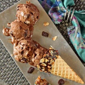 A waffle cone turned on it's side on silver platter with 4 scoops of German Chocolate Brownie Ice Cream laid out in front of it.