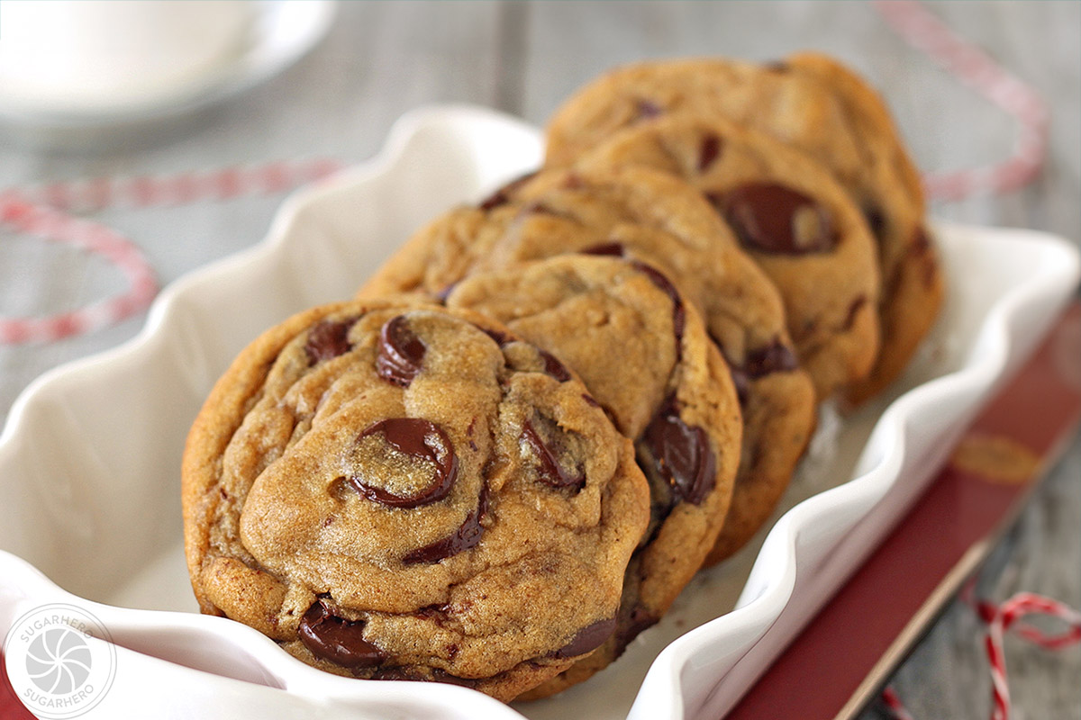Four gingerbread chocolate chip cookies in a rectangle serving plate with scalloped edges placed on a red napkin.
