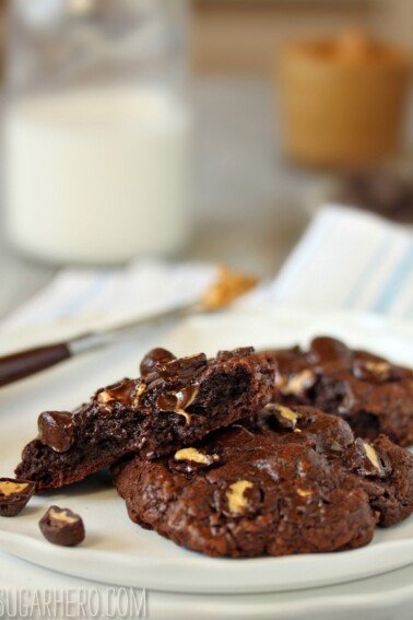 3 Gooey Chocolate Peanut Butter Cup Cookies on a white plate with one cookies broken to show center texture.