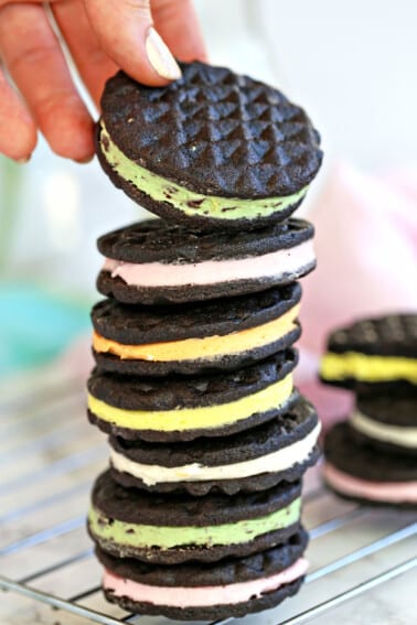 Stack of homemade Oreos with different flavors of filling with a hand pulling one off the top.