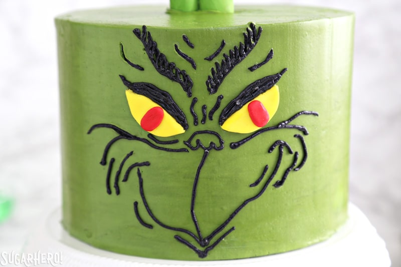 Grinch Cake - close-up of the Grinch's face, done in black buttercream on a green cake | From SugarHero.com