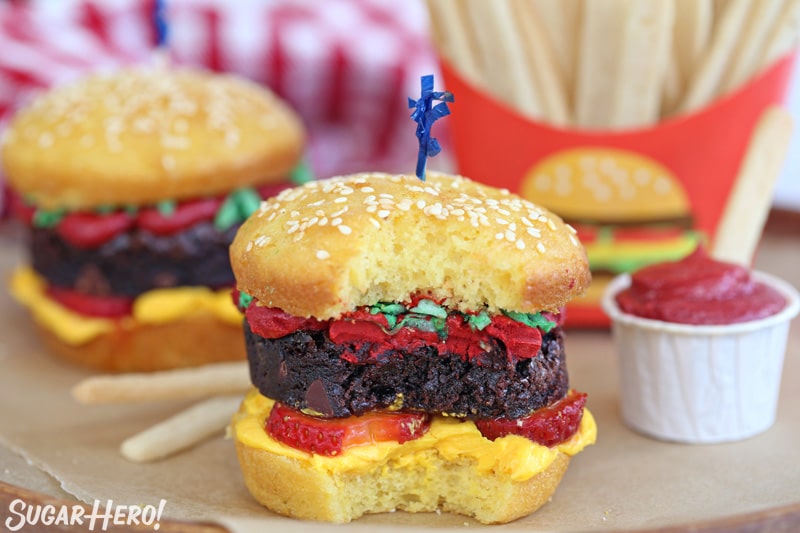 Two hamburger cupcakes, with a bite taken out of the front cupcake