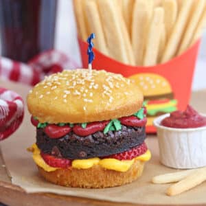 Close-up of Hamburger Cupcake on brown parchment with sugar cookie french fries in the background.