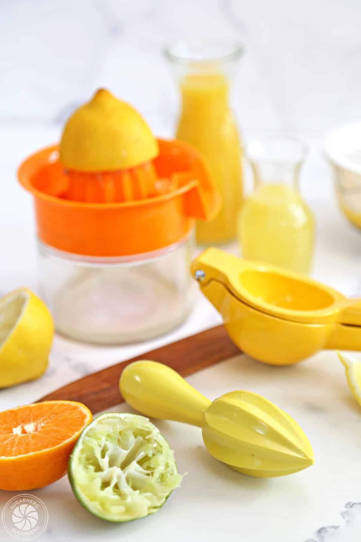 Different citrus juicers on a white marble background with sliced limes, lemons, and oranges around.