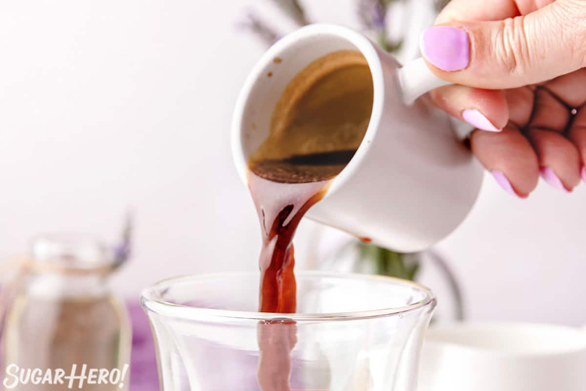 Hand pouring an espresso shot into a clear glass.