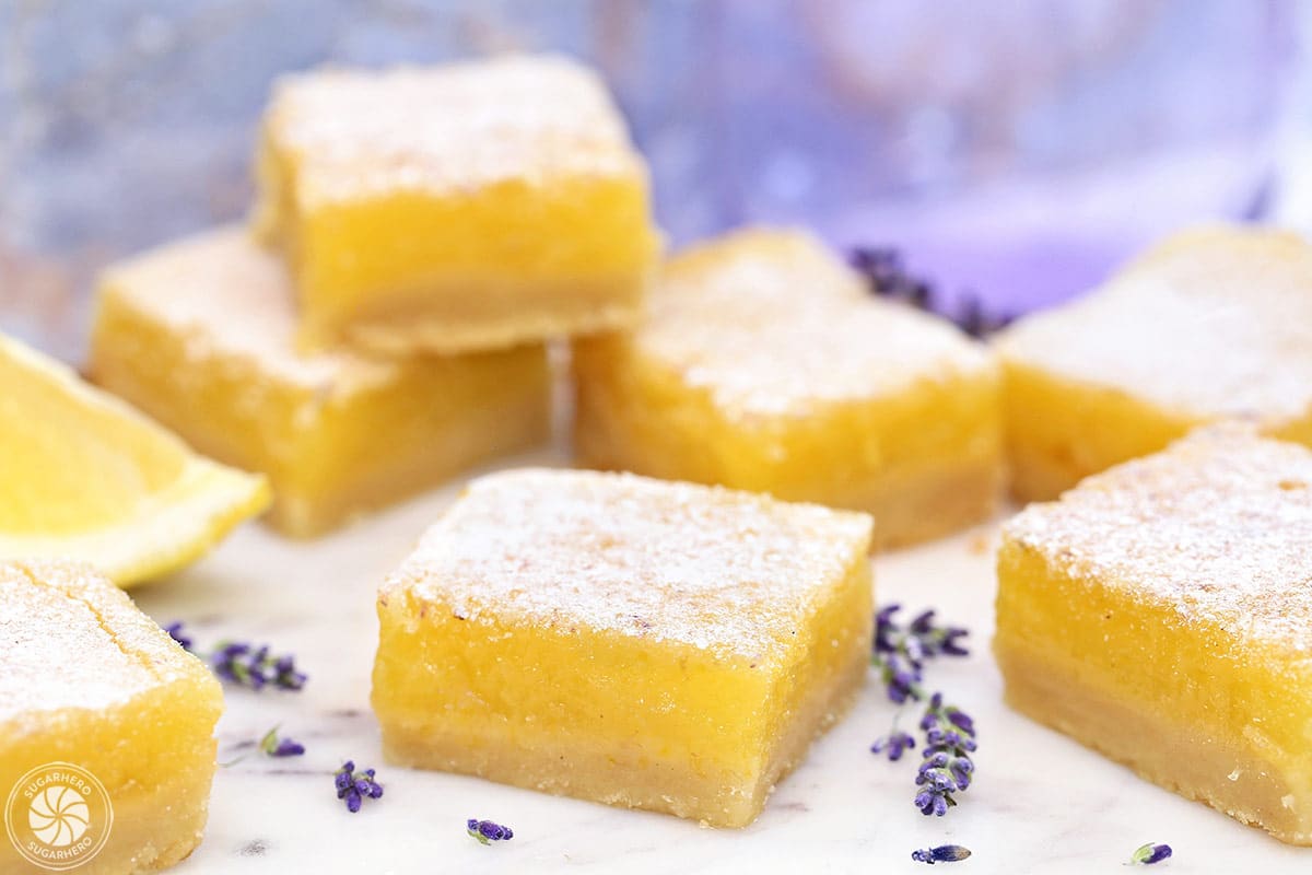 Several cut and stacked Lavender Lemon Bars next to lavender buds.