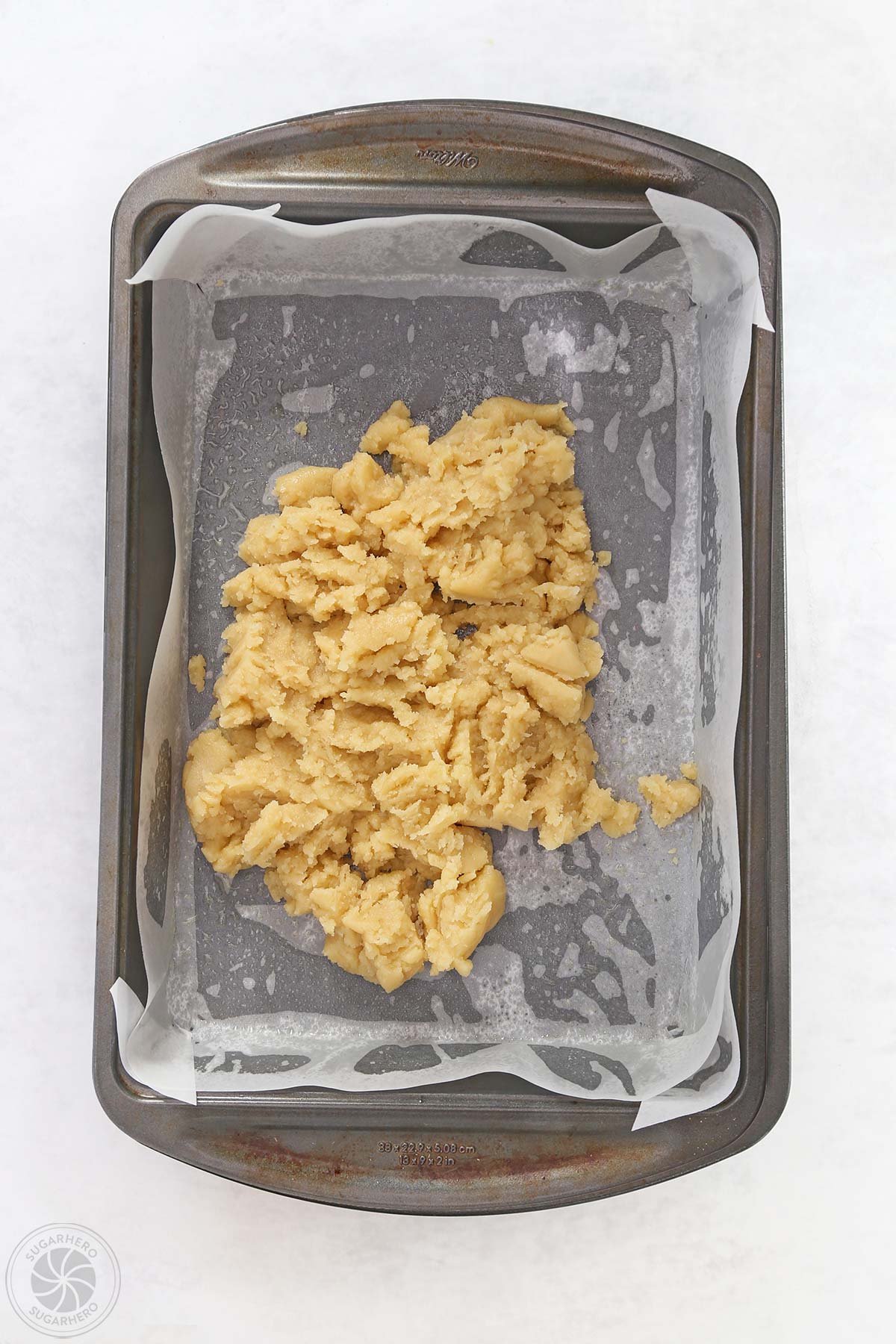 A metal baking pan lined with parchment and a pile of dough.