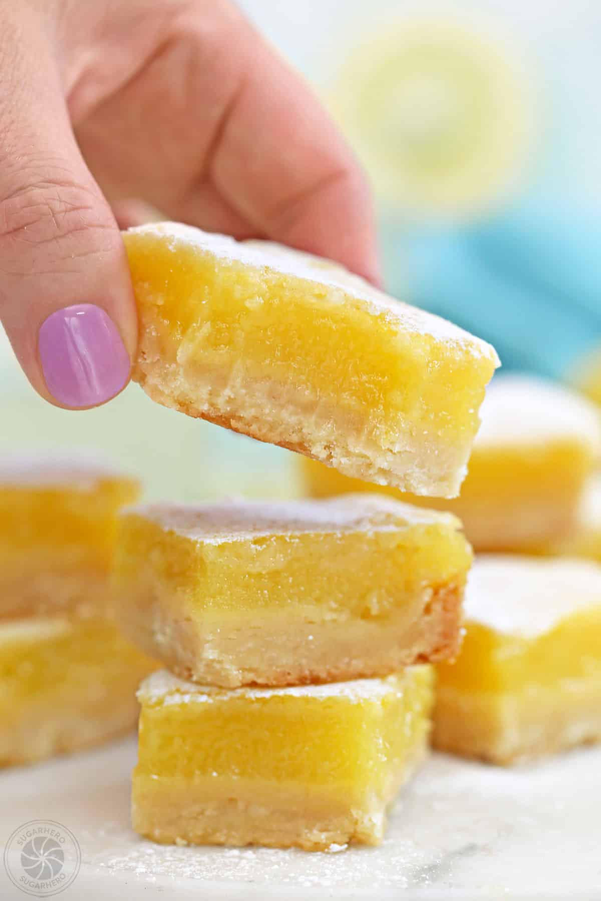 Hand picking up a lemon bar from a stack.