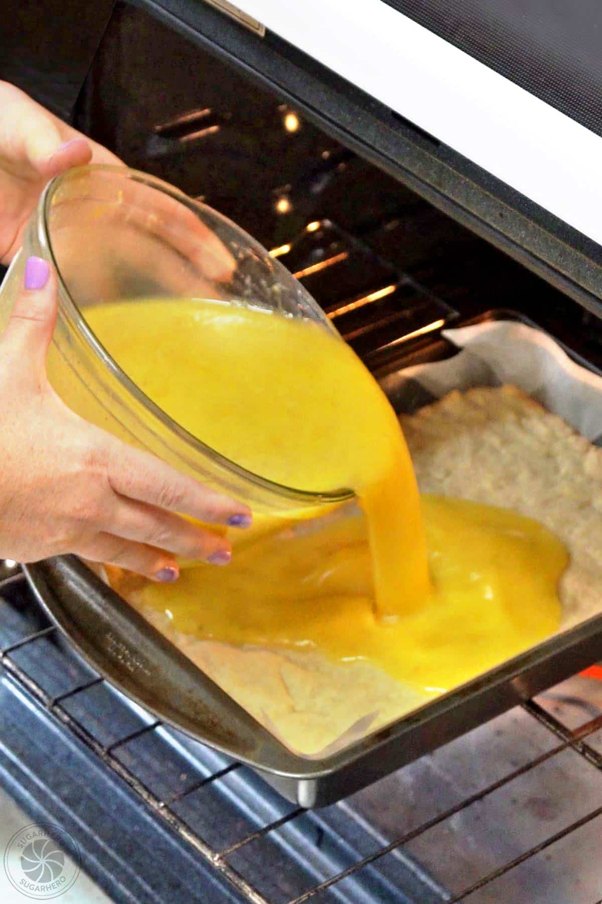 Hands pouring lemon bar filling over partially backed crust in the oven.