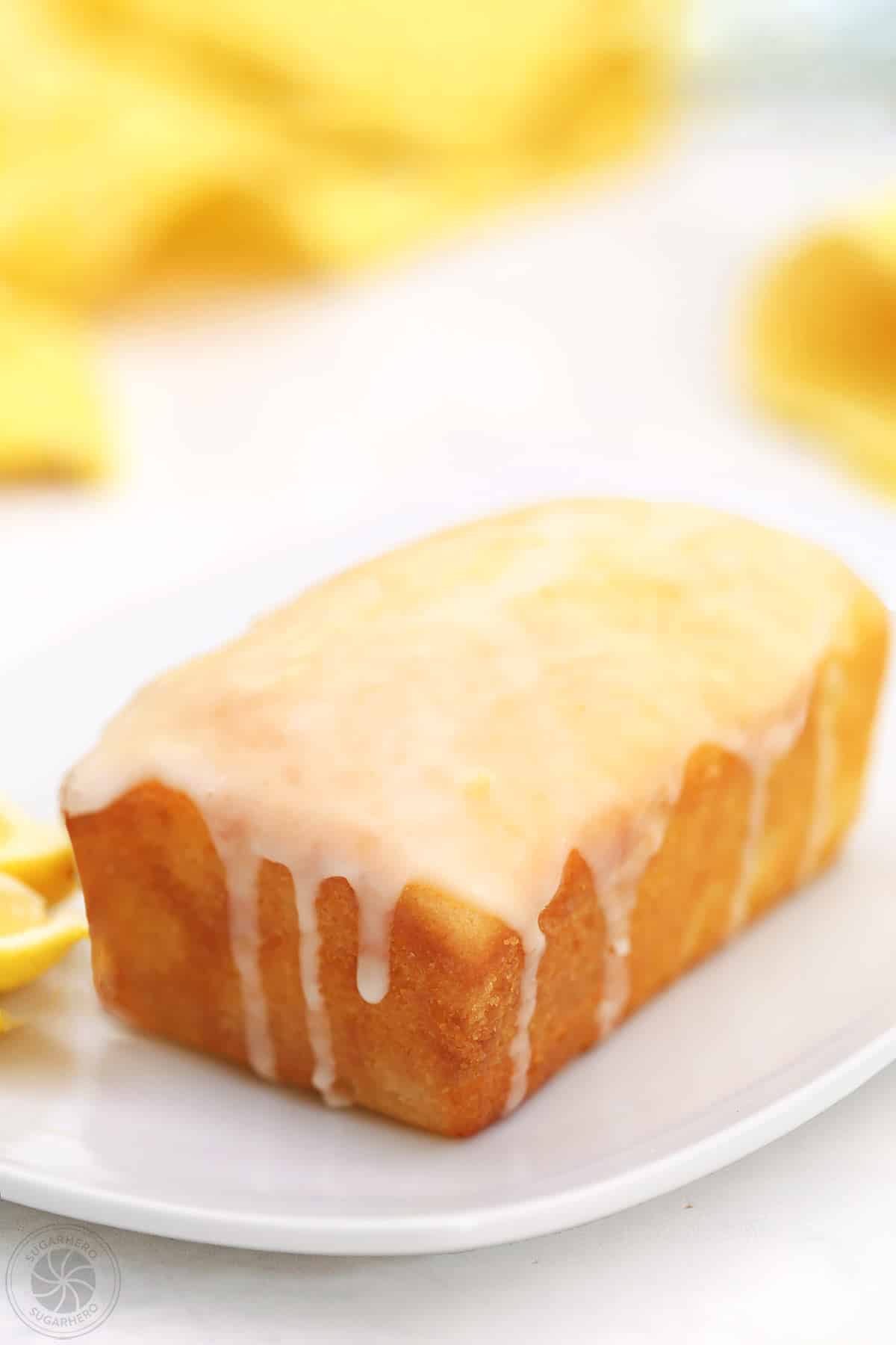 Glazed lemon bread loaf on a white place, with a yellow napkin in the background.