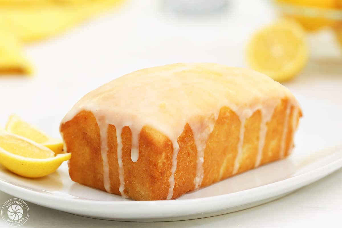 Glazed lemon bread loaf on a white place, with cut lemons in the background.