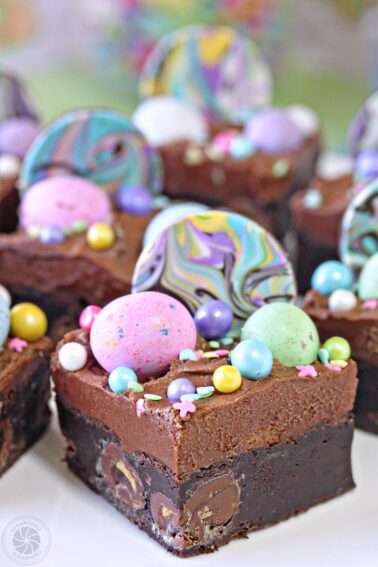 Close up of seven Frosted Easter Brownies covered in chocolate frosting and topped with chocolate eggs and sprinkles.