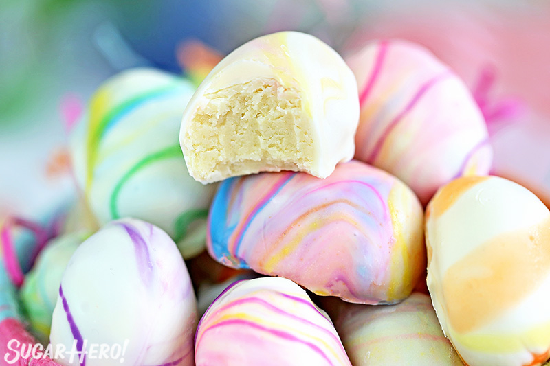 Close-up of white chocolate truffle with a bite taken out of it, on a pile of Marbled Easter Egg Truffles.