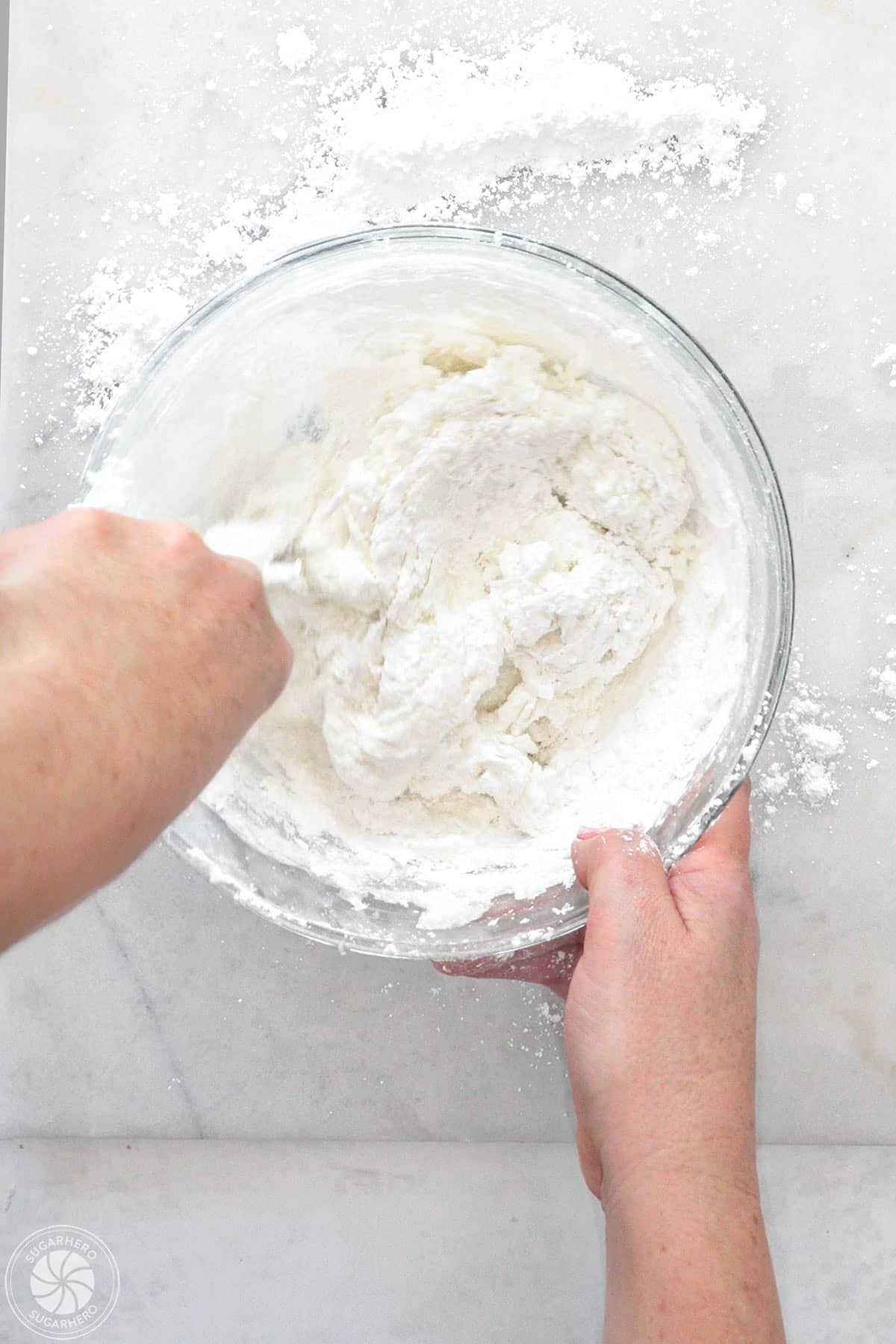 Hand stirring powdered sugar into a bowl of fondant.